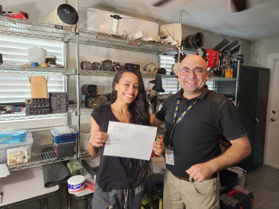 Smiling A&P graduate holding her FAA certificate with her instructor