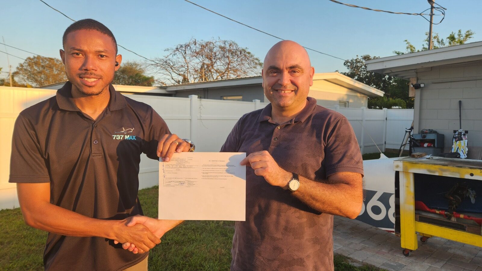 A recently certified A&P student shaking hands with instructor Kivilcim Ozaner, holding a freshly issued FAA certificate beside an aircraft